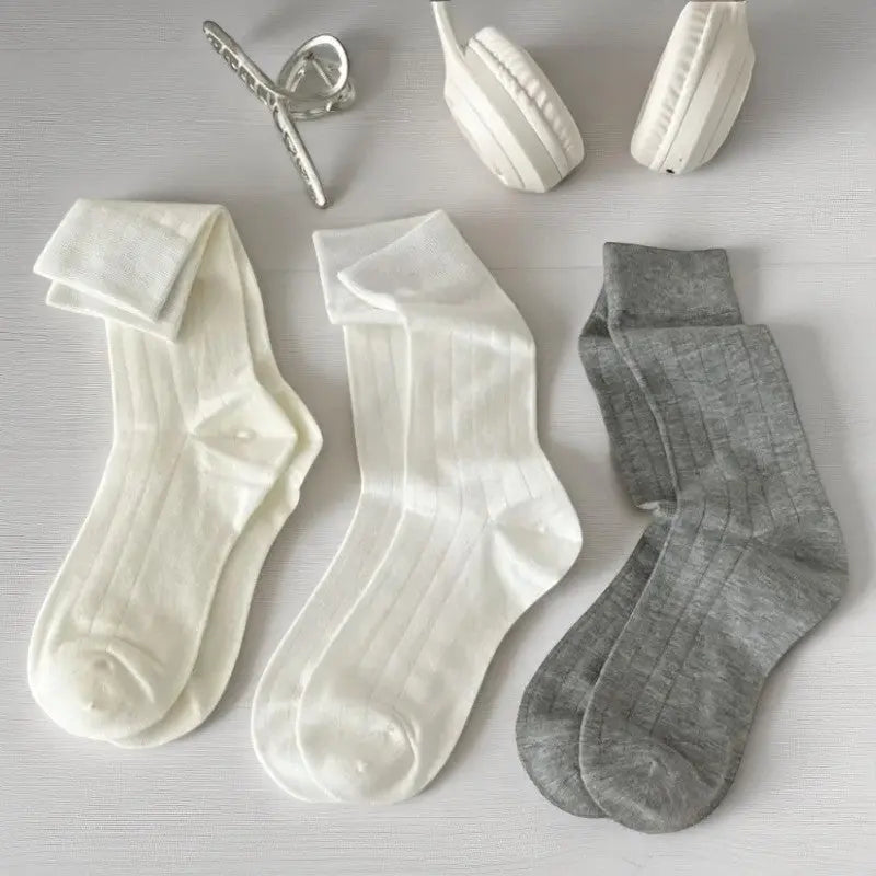 Trois paires de chaussettes en bambou pour femme (deux blanches, une grise), avec accessoires blancs.