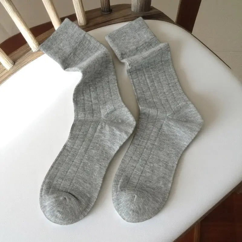 Paire de chaussettes grises en bambou côtelé, posée à plat sur une chaise en bois clair.