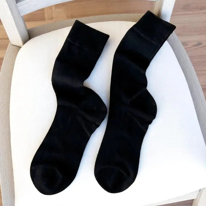 Paire de chaussettes noires en bambou pour femme, à plat sur une chaise en bois et tissu clair.