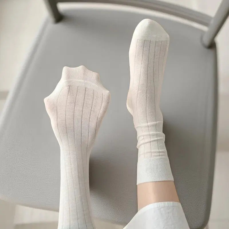 Gros plan sur les chaussettes blanches en bambou côtelé, portées par une femme allongée sur chaise.