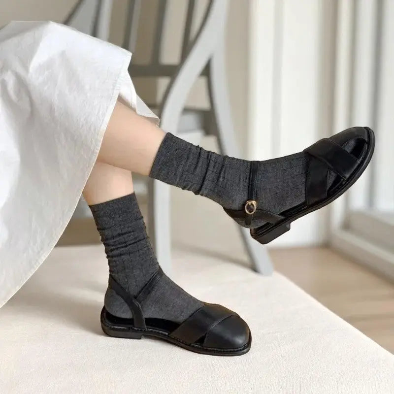 Femme portant des chaussettes en bambou gris foncé avec sandales noires, vue assise élégante.