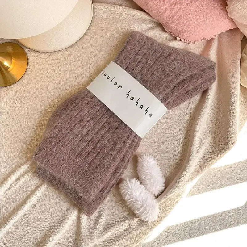 Chaussette en cachemire rose poudré posée sur un lit beige avec une lumière naturelle.