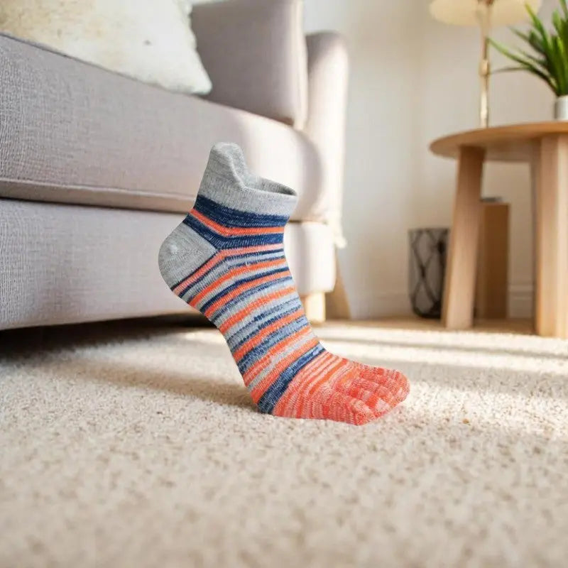 Chaussettes à doigts de pied rayées grises, oranges et bleues pour homme posées sur un tapis.
