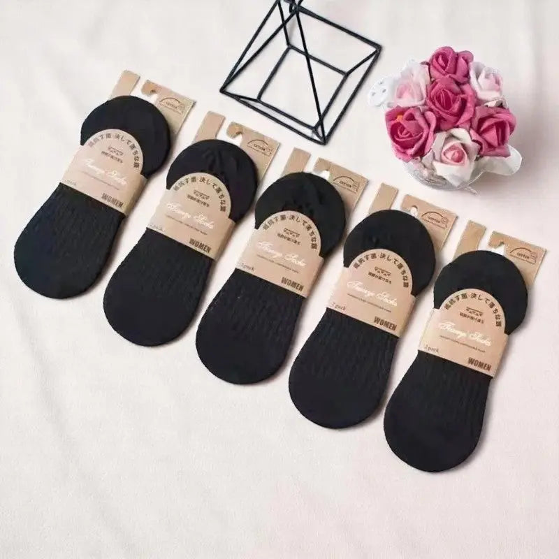 Lot de chaussettes invisibles noires pour femme sur fond beige doux, accompagnées d’un bouquet de roses.