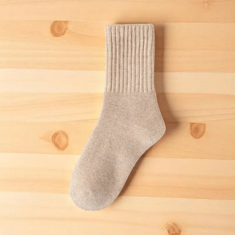 Chaussette beige clair en laine posée sur un fond bois naturel.