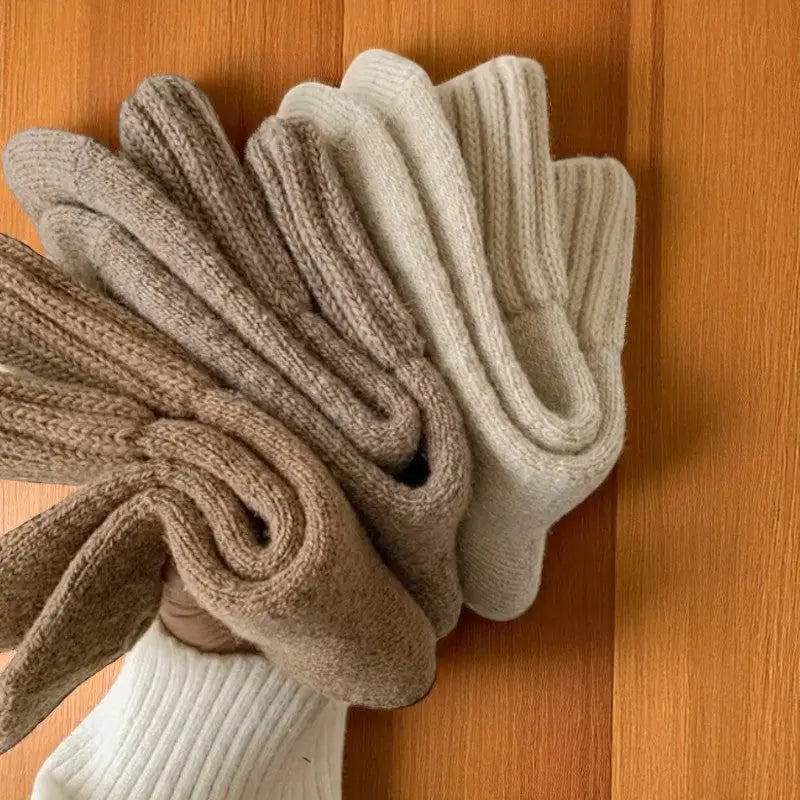 Trois paires de chaussettes en laine beige et marron tenues à la main.