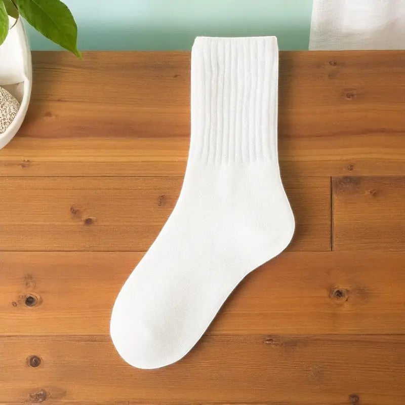 Chaussette en laine blanche posée à plat sur une planche en bois.