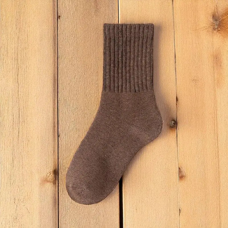 Chaussette marron foncé en laine posée sur du bois brut.