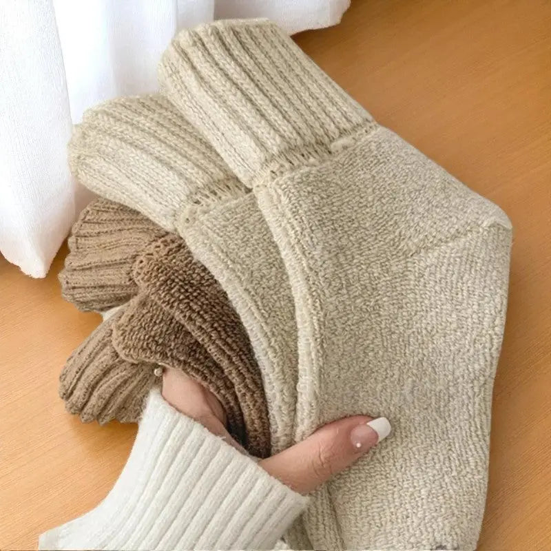 Gros plan sur des chaussettes laineuses dans une main vêtue d’un pull blanc.