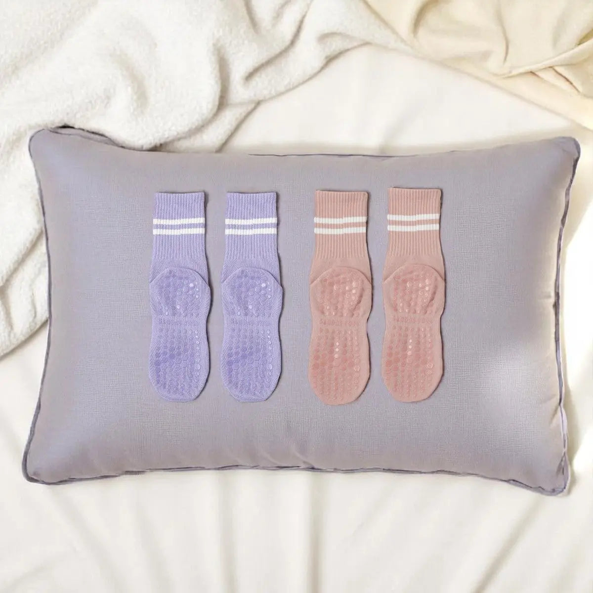 Lot de chaussettes antidérapantes femme violet lilas et rose poudré posées sur un coussin gris.