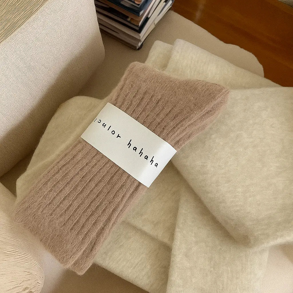 Paire de chaussettes en cachemire beige posée sur une couverture duveteuse, ambiance chaleureuse.