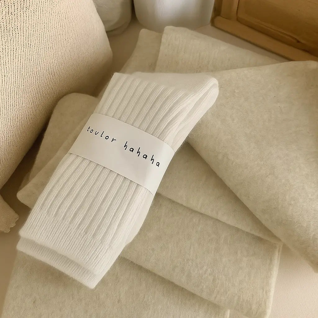 Chaussettes blanches en cachemire soigneusement pliées sur un fond crème moelleux.