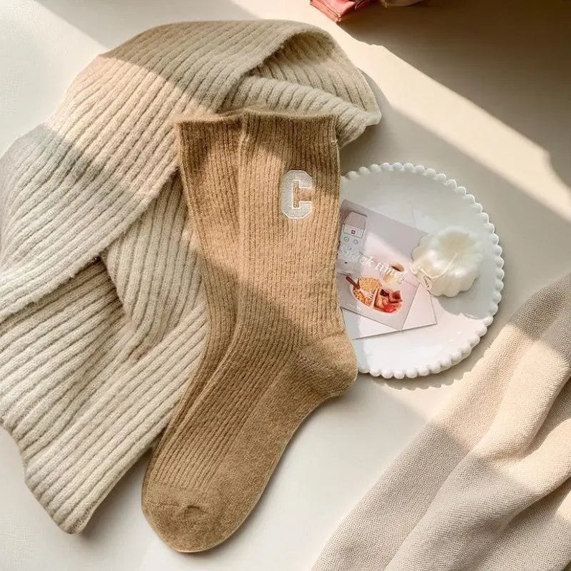 Chaussettes en cachemire camel pour femme posées sur un plateau blanc, ambiance cocooning douce et lumineuse.
