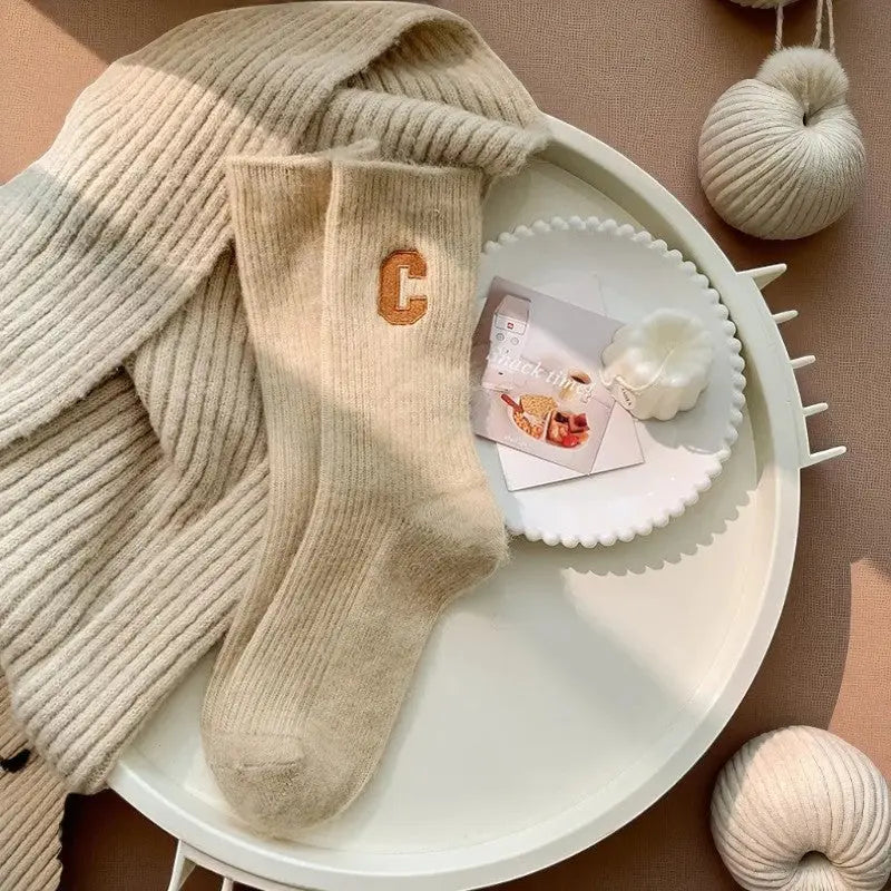 Paire de chaussettes en cachemire pour femme, camel clair posée sur plaid beige.