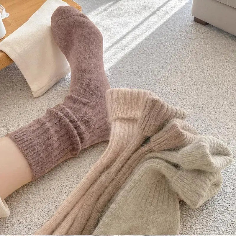 Chaussette en cachemire mauve portée au pied, avec d'autres paires posées au sol dans une lumière douce.