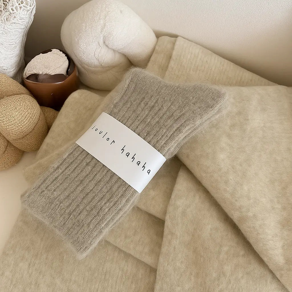 Paire de chaussettes cachemire gris perle sur un plaid clair avec objets de décoration cocooning.