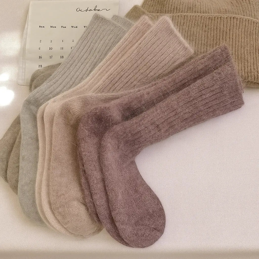 Chaussettes en cachemire dans des tons naturels posées sur un fond beige avec calendrier d'octobre.