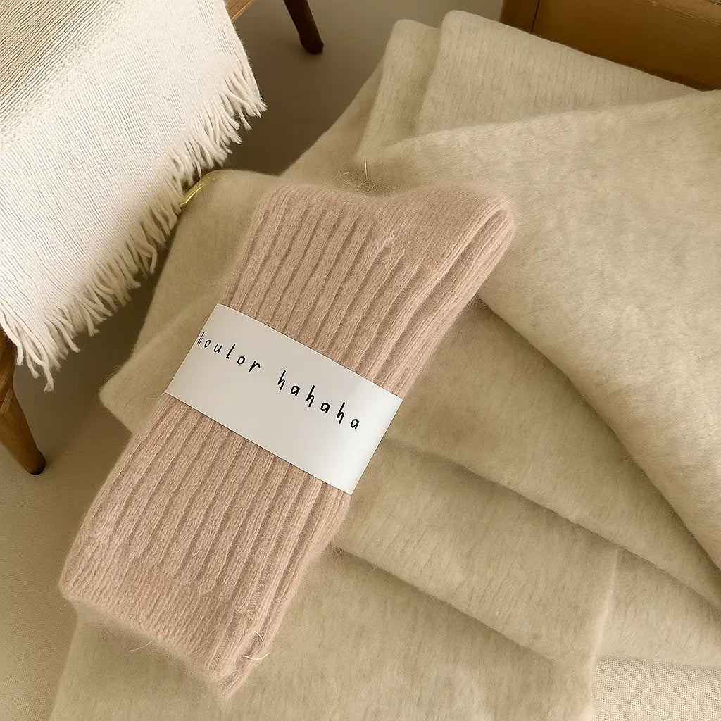 Chaussettes en cachemire rose poudré posées sur un fond beige texturé, ambiance douce et élégante.