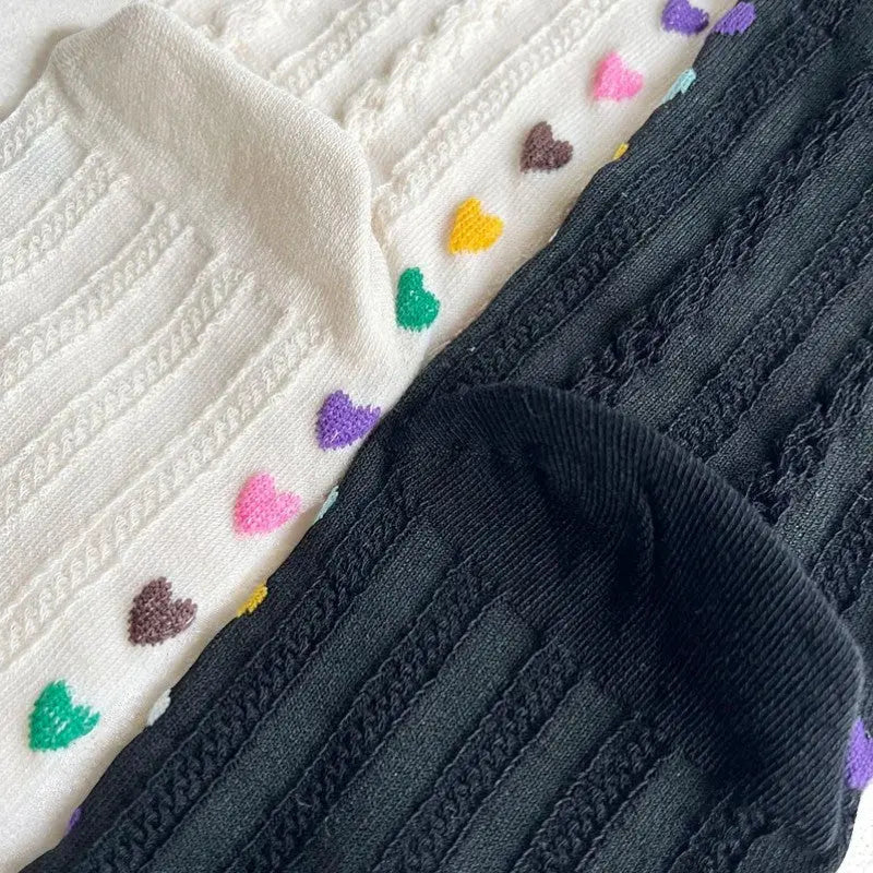 Détail des chaussettes à doigts noires et blanches avec petits cœurs multicolores.