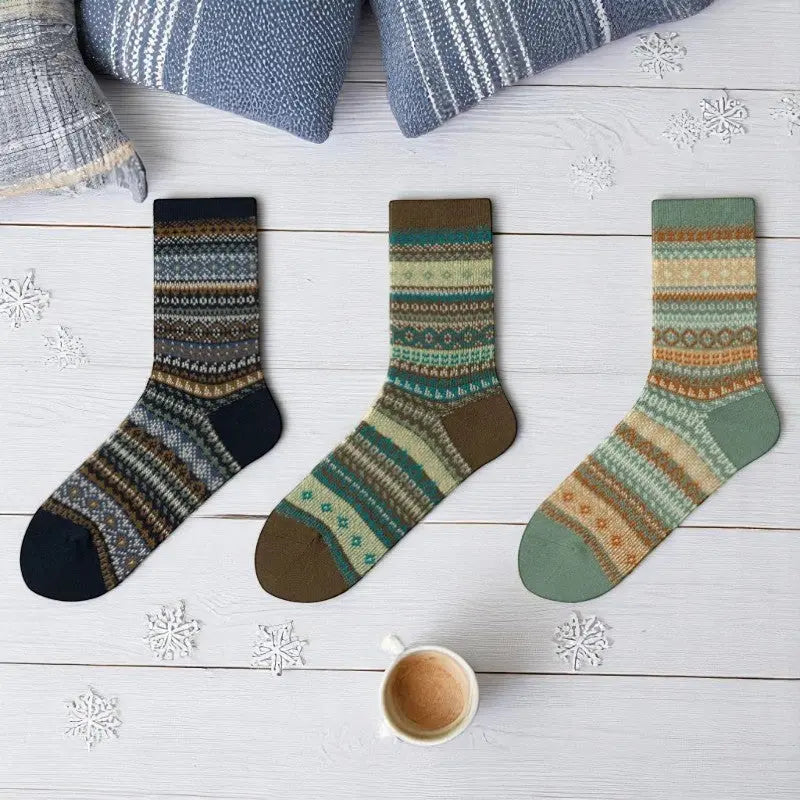 Chaussettes hivernales femme aux nuances de bleu, vert et beige disposées près d’un mug chaud sur un sol clair.