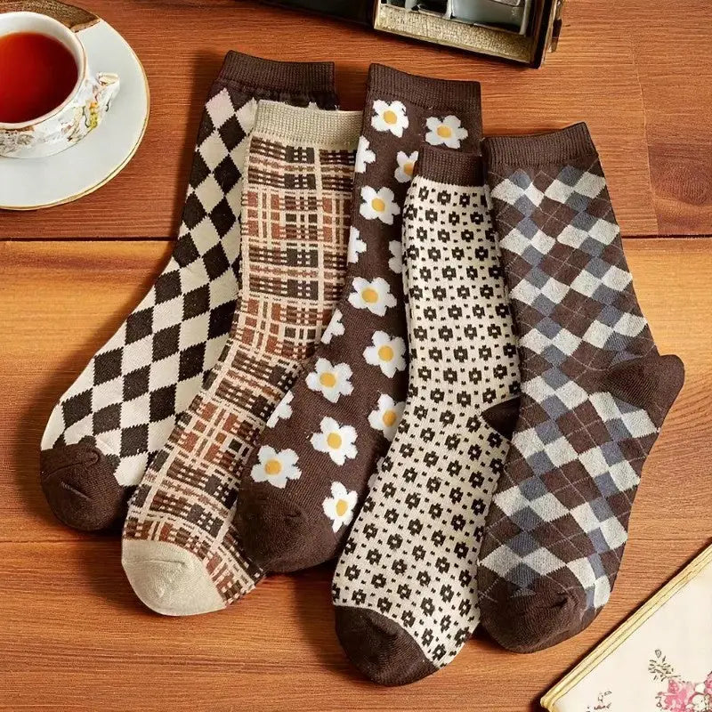 Lot de cinq paires de chaussettes rétro-chic pour femme, aux motifs floraux, géométriques et écossais, sur fond en bois.