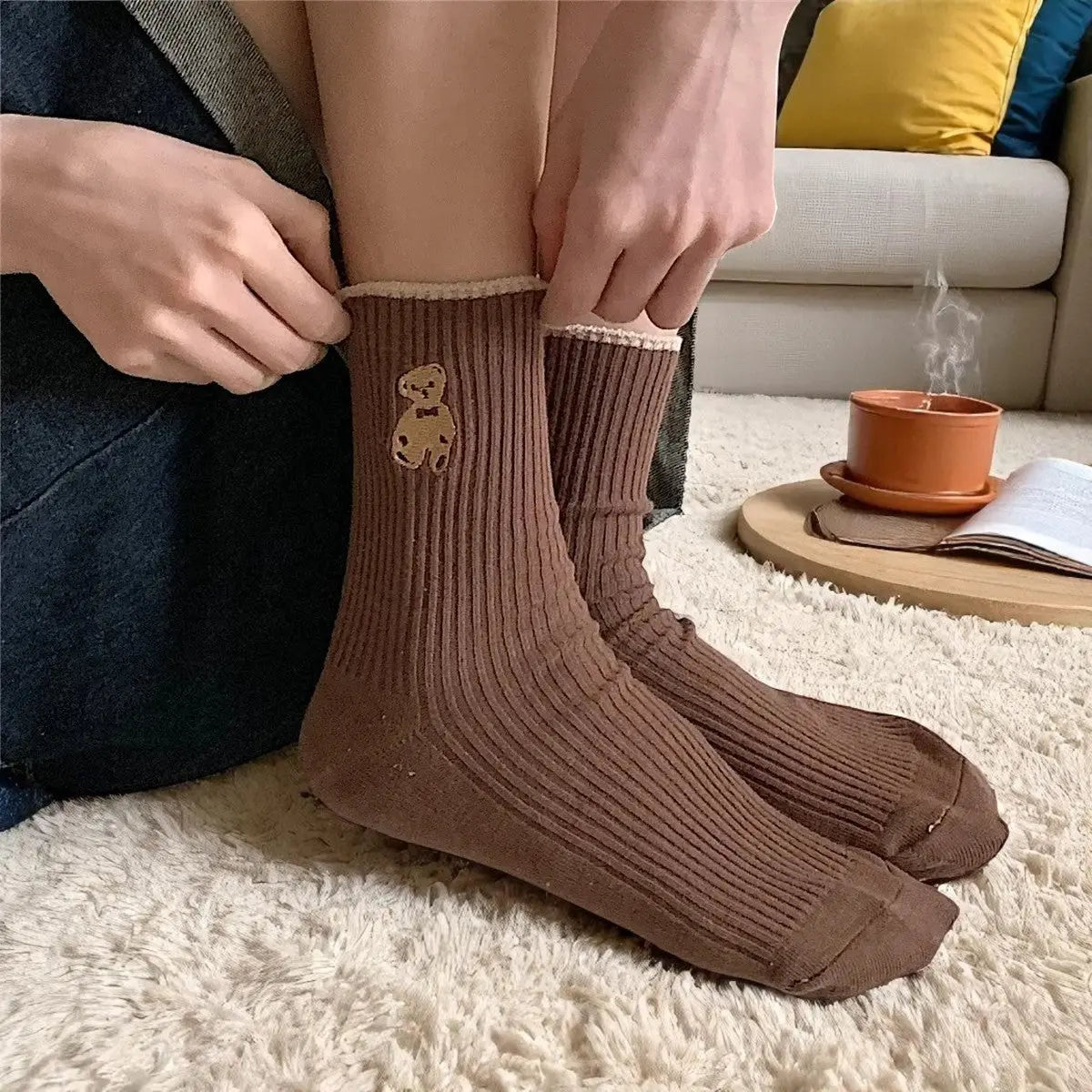 Chaussettes marron chocolat avec ourson, portées dans un intérieur cosy avec tasse et livre.