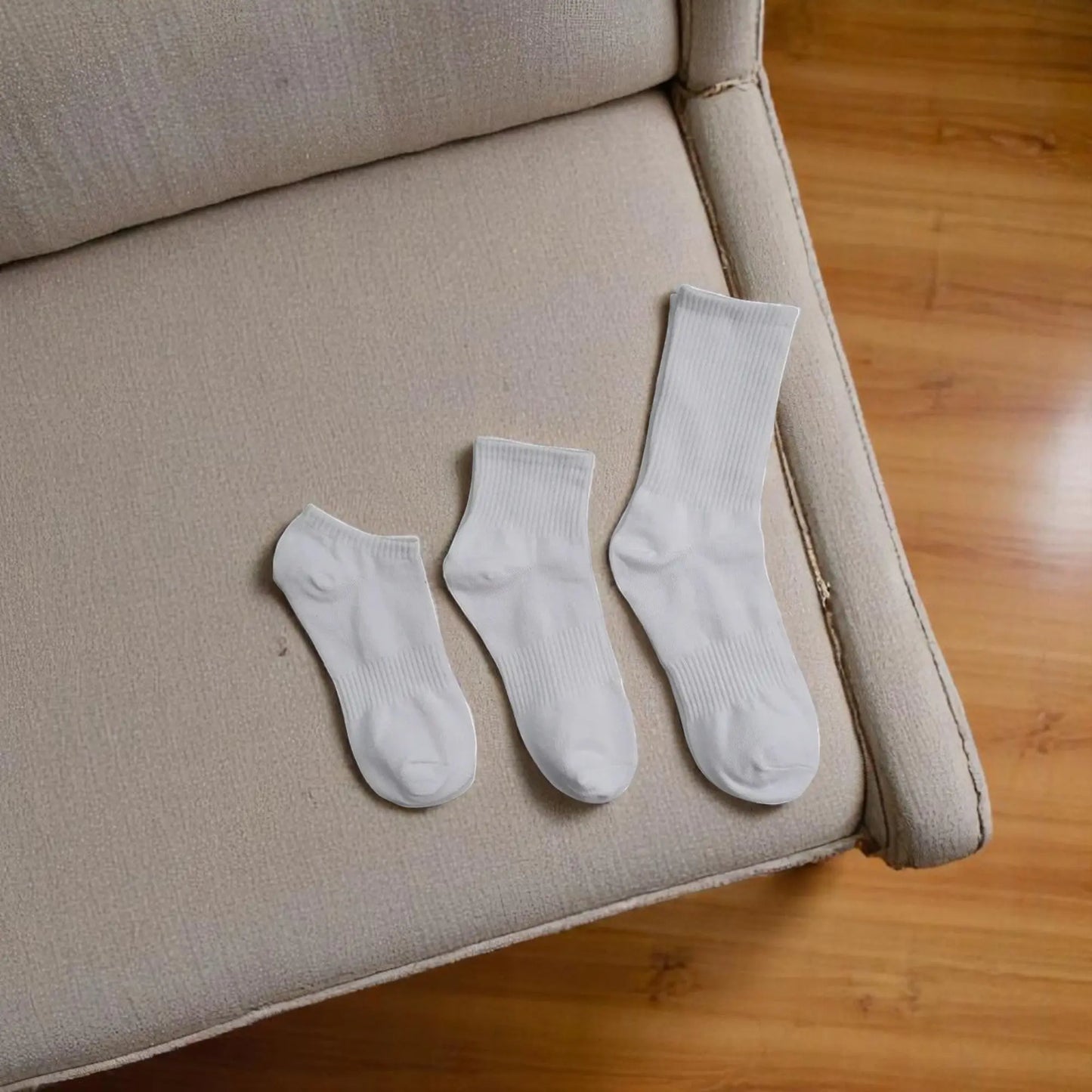 Trois paires de chaussettes blanches antitranspirantes pour homme de différentes longueurs posées sur un canapé.