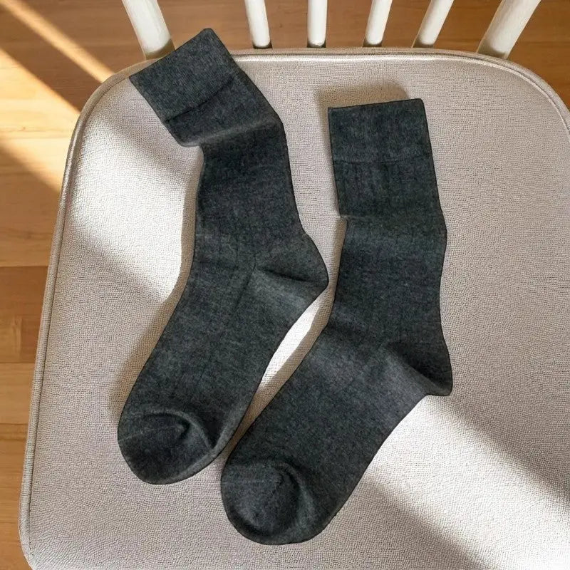 Chaussettes en bambou gris foncé pour femme, allongées sur une chaise crème avec lumière naturelle.