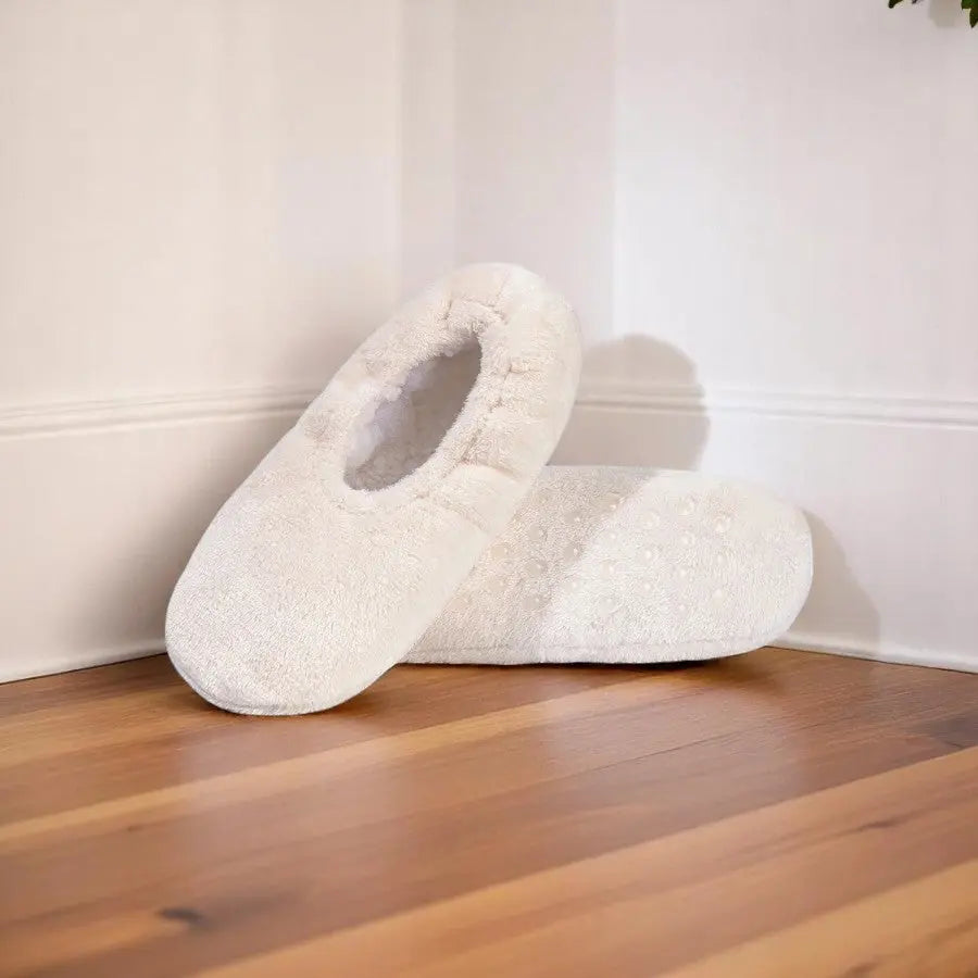 Chaussettes chaussons crème beiges douces et confortables pour femme, posées sur sol bois clair.