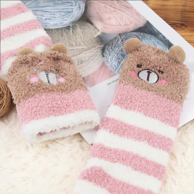 Chaussettes hautes rose et blanc à motif ours, posées sur des pelotes de laine pastel.