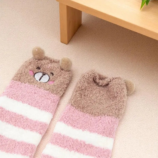 Détail de chaussettes hautes pliées rose et blanc, décor visage d’ours brodé.