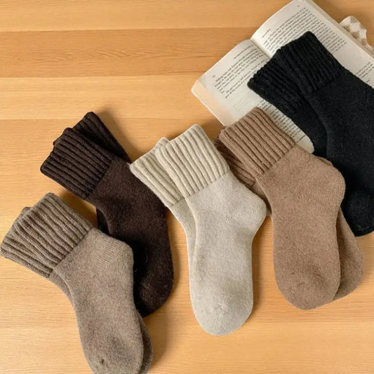 Lot de chaussettes en laine aux tons chauds disposé à côté d’un livre ouvert.