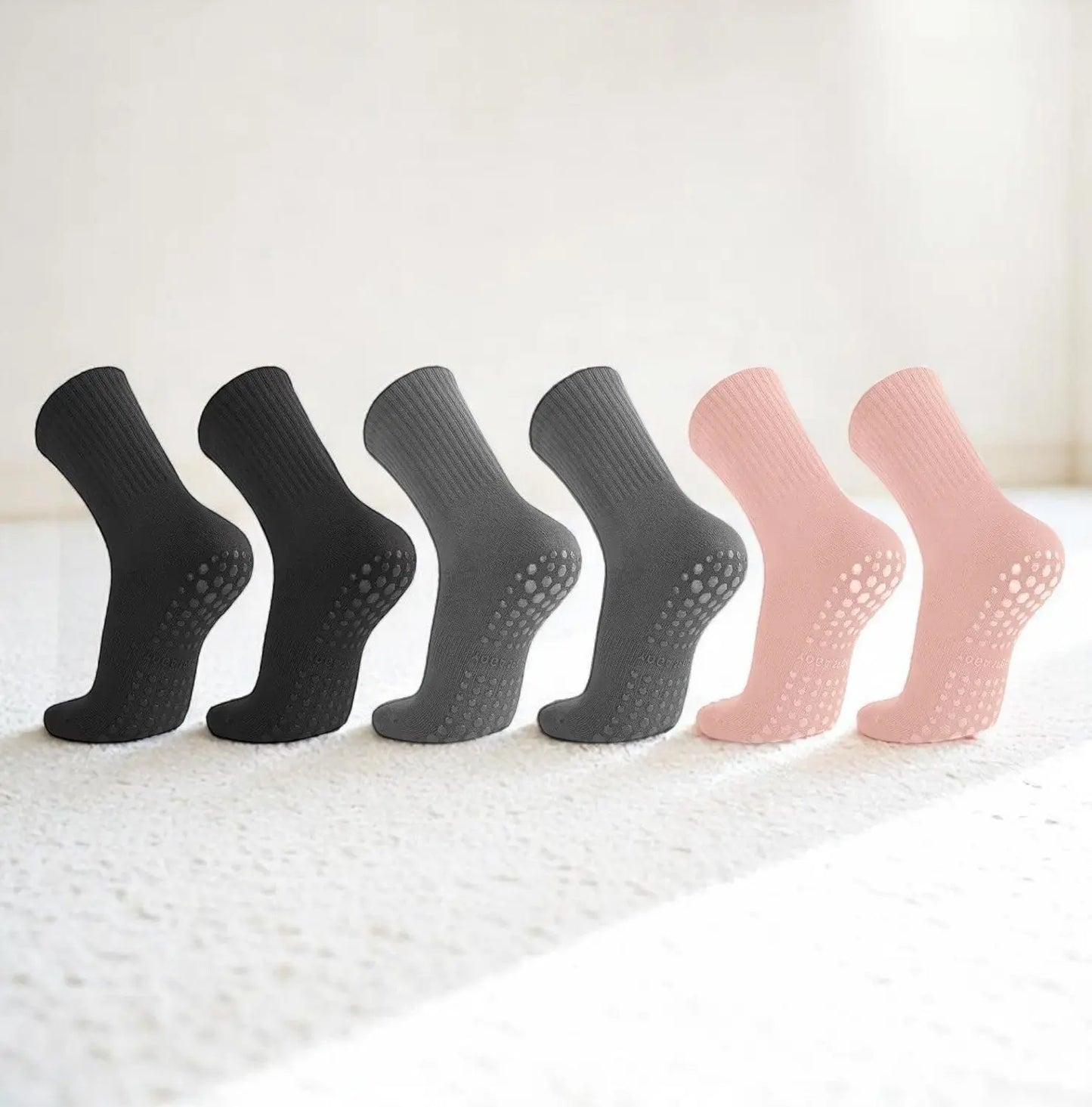 Chaussettes antidérapantes femme en noir, gris et rose posées en ligne sur moquette claire.