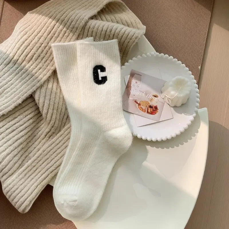 Chaussettes cachemire blanches pour femme avec lettre C noire posées sur plaid beige.
