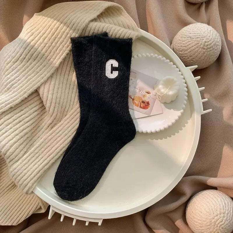 Chaussettes cachemire noires pour femme avec lettre C blanche dans un décor cocooning.