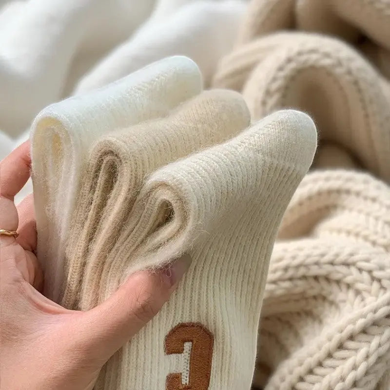 Lot de trois chaussettes cachemire pour femme pliées (blanc, crème, beige) en main.