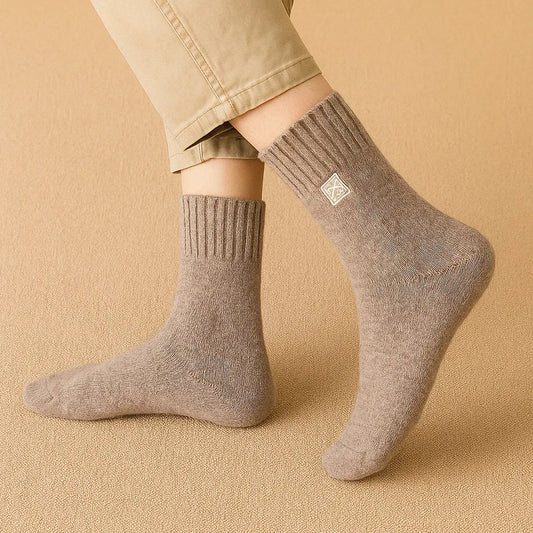 Homme portant une paire de chaussettes en cachemire beige sur un tapis texturé.