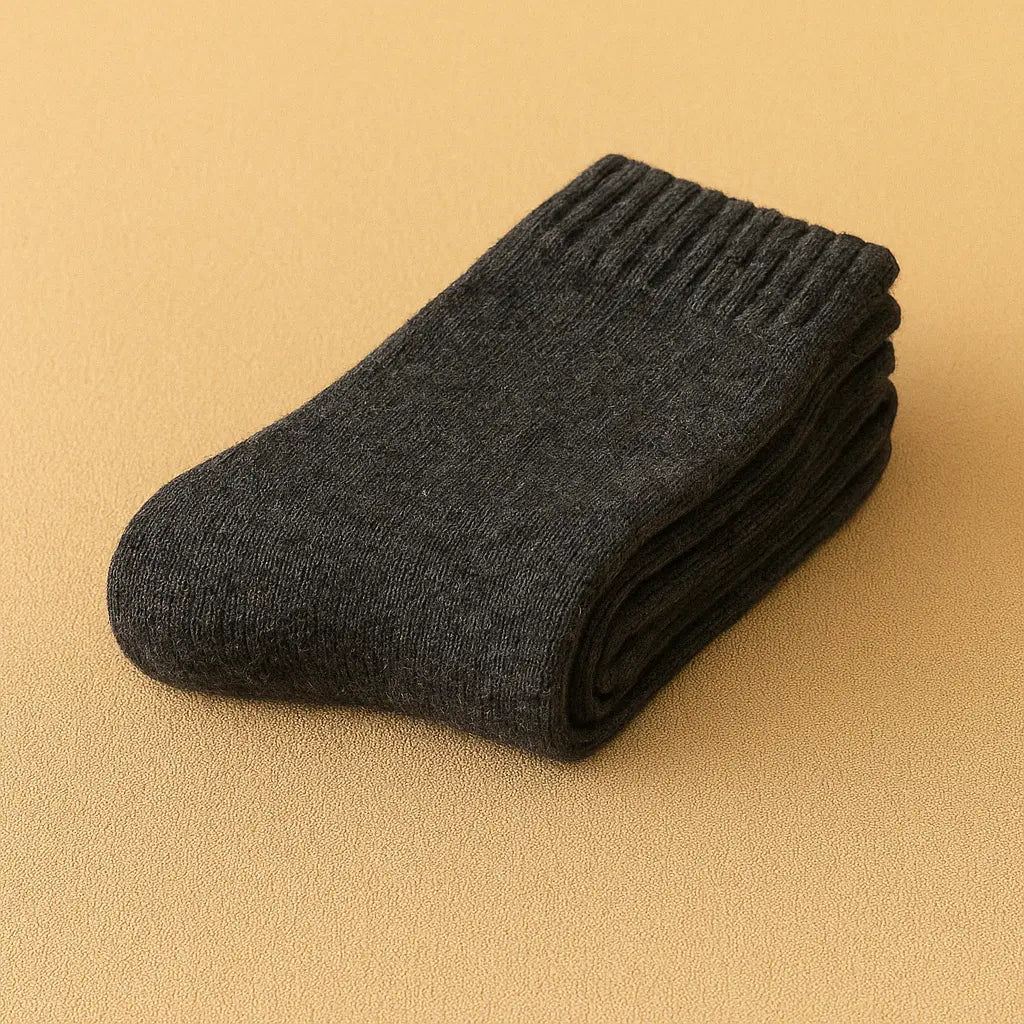 Chaussettes pour homme en cachemire gris foncé, posées soigneusement sur un fond beige doux.