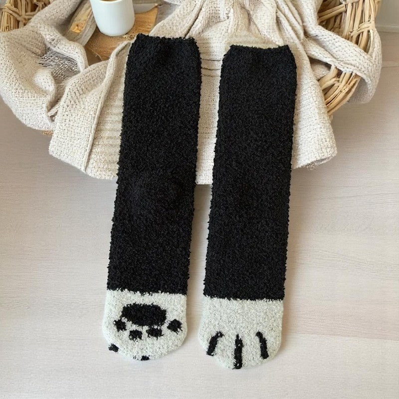 Paire de chaussettes noires et blanches façon patte de chat posées sur un panier en rotin.