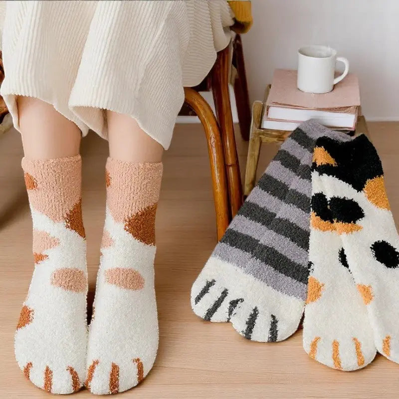 Chaussettes félines douillettes portées avec des livres et une tasse dans un coin cocooning.
