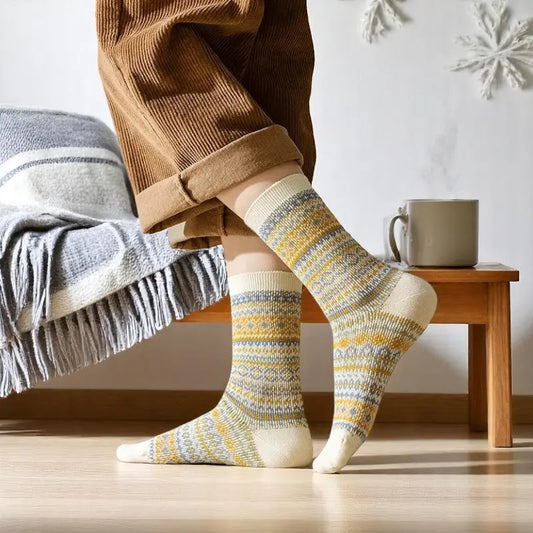 Chaussettes style norvégien jaune et grises portées avec un pantalon en velours dans un décor douillet.