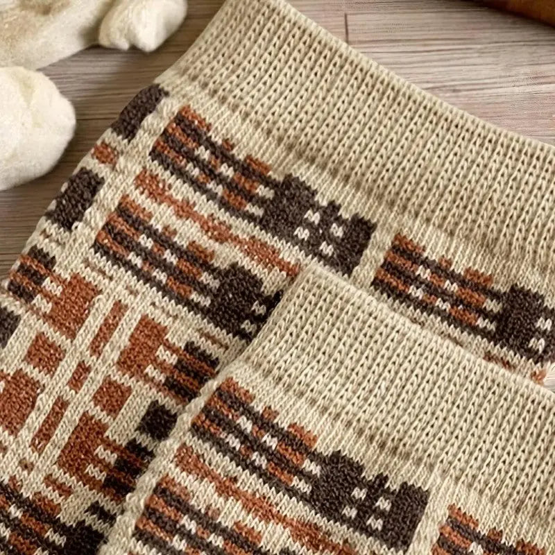 Gros plan sur une paire de chaussettes d’hiver à motif écossais dans des tons chauds, posée sur un parquet clair.
