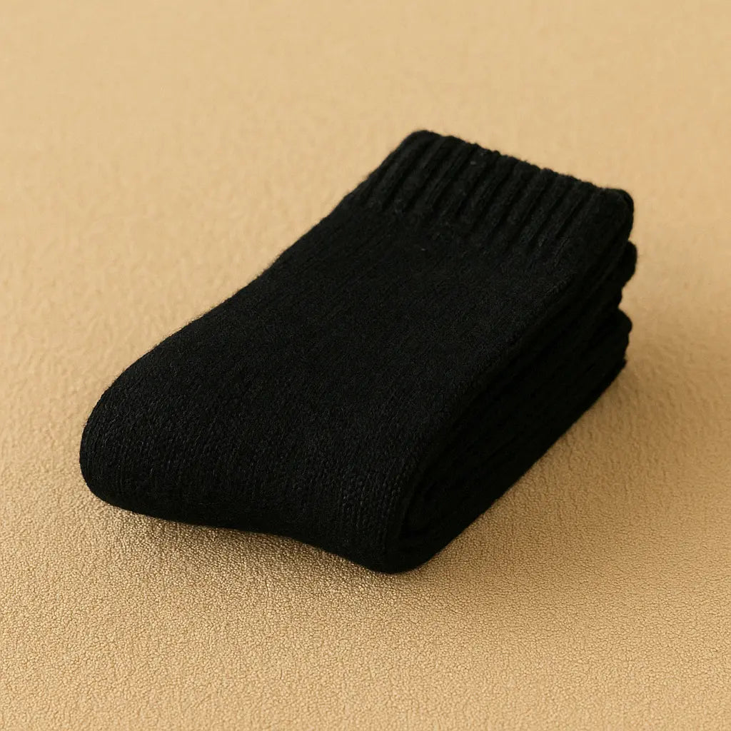 Paire de chaussettes en cachemire noires pour homme, élégamment pliée sur un tapis beige.
