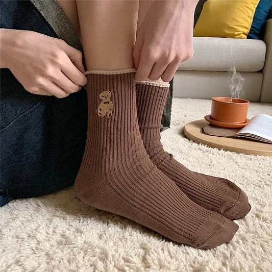 Chaussettes marron chocolat avec ourson, portées dans un intérieur cosy avec tasse et livre.