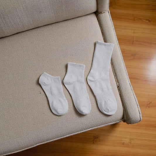 Trois paires de chaussettes blanches antitranspirantes pour homme de différentes longueurs posées sur un canapé.