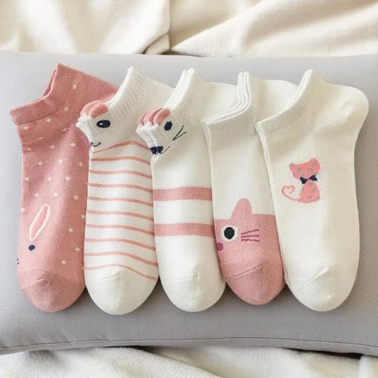  Cinq socquettes roses et blanches aux motifs chat posées sur un coussin gris clair.