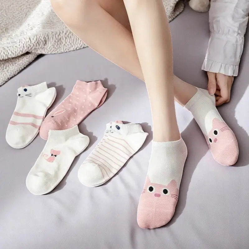 Lot de cinq socquettes blanches et roses avec motifs chat et rayures pastel, posées sur lit.