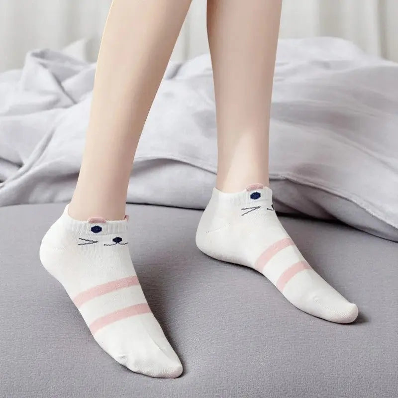 Socquettes blanches aux détails de museau et oreilles de chat portées sur un lit.